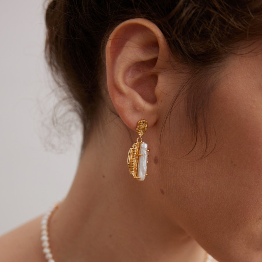 Model wearing auric pearl statement earrings with elegant warm-toned styling
