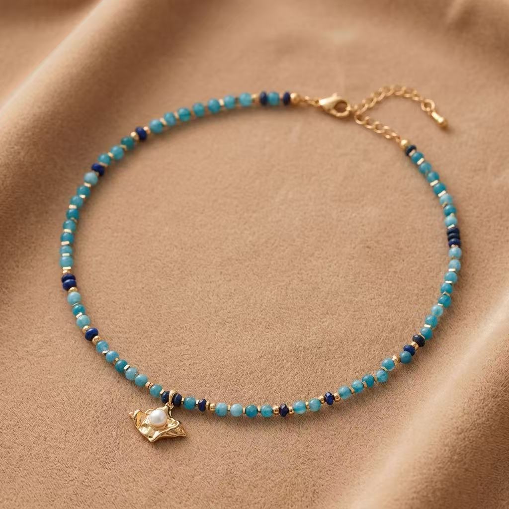 Lapis lazuli beaded necklace with pearl pendant and vintage gold details on warm fabric